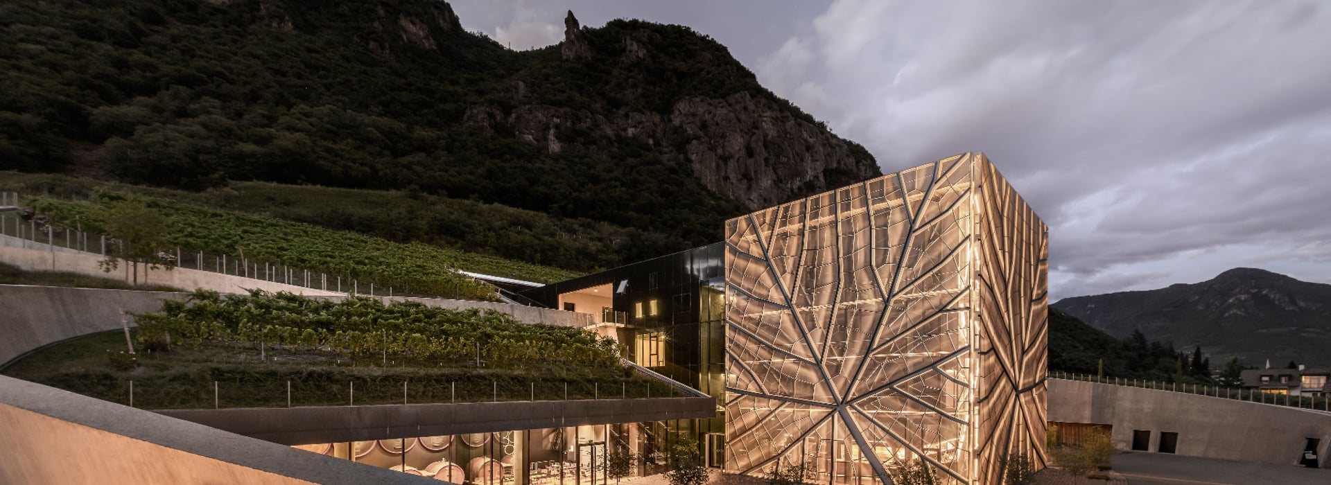 Cantina di Bolzano-Gries con architettura moderna e particolare al crepuscolo, illuminata sotto un cielo scuro.