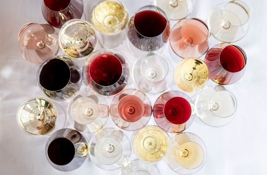 Molti calici da vino disposti uno accanto all’altro, fotografati dall’alto. Si distinguono diversi vini: bianchi, rossi, spumanti e rosé, ognuno servito in un bicchiere diverso.