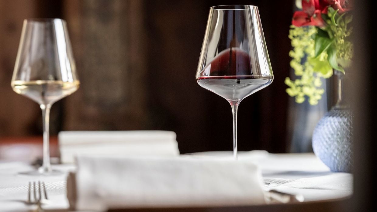 Due calici di vino, uno bianco e uno rosso, su un tavolo in una vecchia stube, accanto un vaso di fiori.