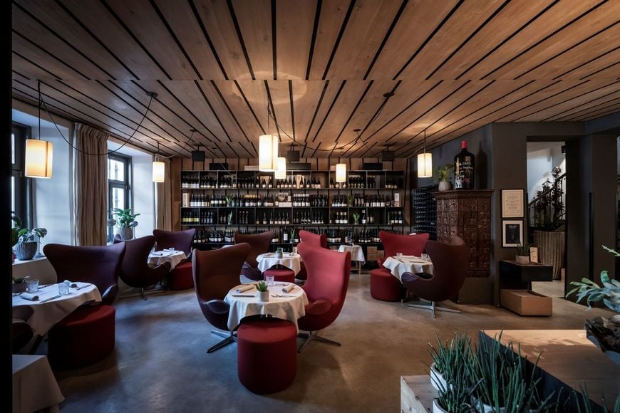 Interno del ristorante con tavoli apparecchiati, poltrone accoglienti e una grande esposizione di vini sullo sfondo. ©Löwengrube/Alex Filz